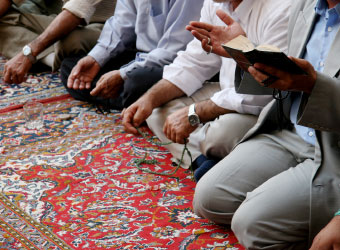 Männer knien auf einem großen Gebetsteppich.