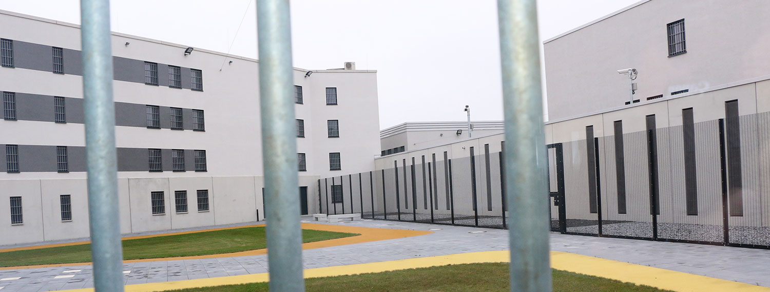 Blick durch Gitterstäbe in einen Gefängnishof.